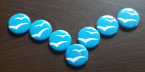 Siete chapas azules con el logo de las gaviotas de Apache OpenOffice, colocadas en forma de V sobre una mesa de madera